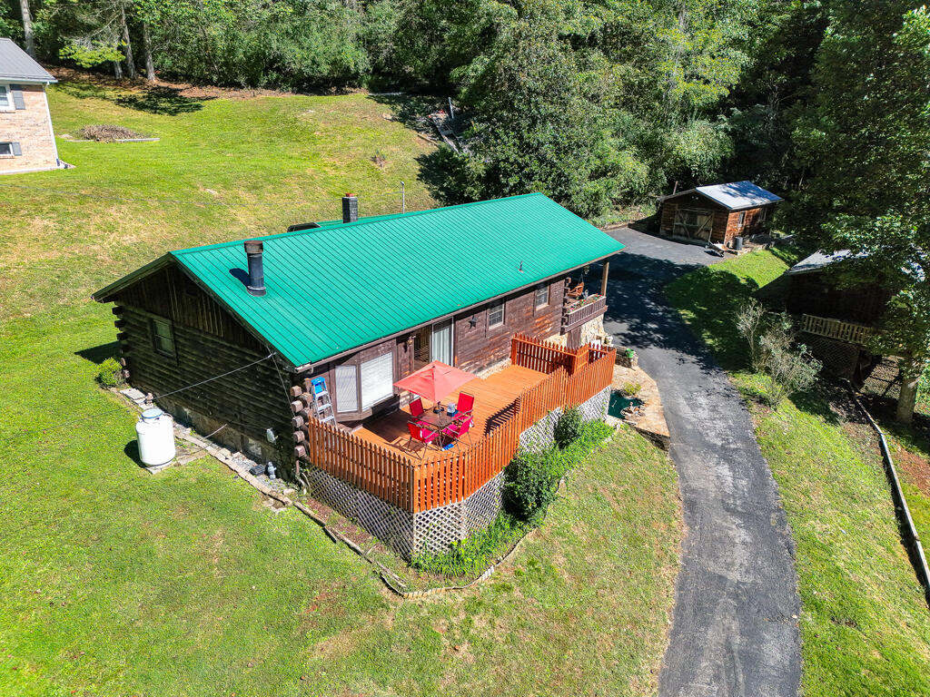 Rustic log cabin with teal roof and fenced patio deck, viewed from above.