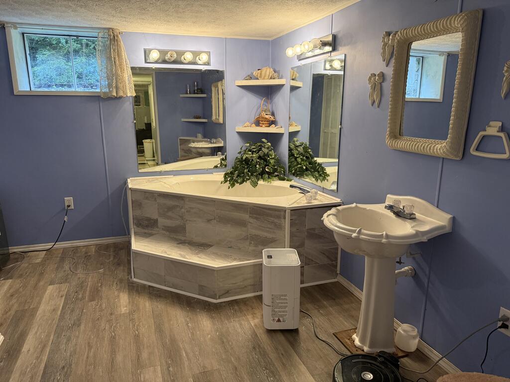 Bathroom with a large tiled corner soaking tub, pedestal sink, and lavender walls.