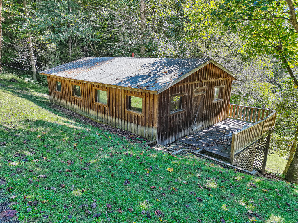 Wood-sided house on a wooded slope with a raised deck and weathered metal roof.
