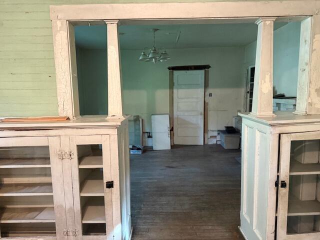 Vacant room seen through worn built-in cabinets, with a chandelier and paneled door.