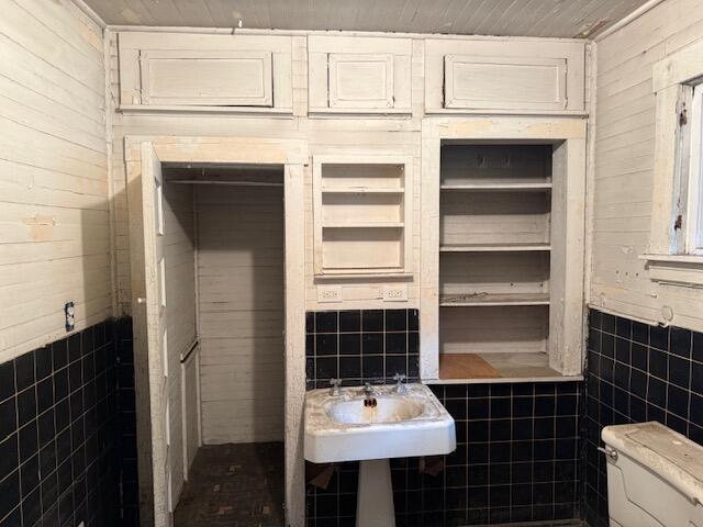Bathroom with black tile walls, a pedestal sink, open built-in shelves, and part of a toilet.
