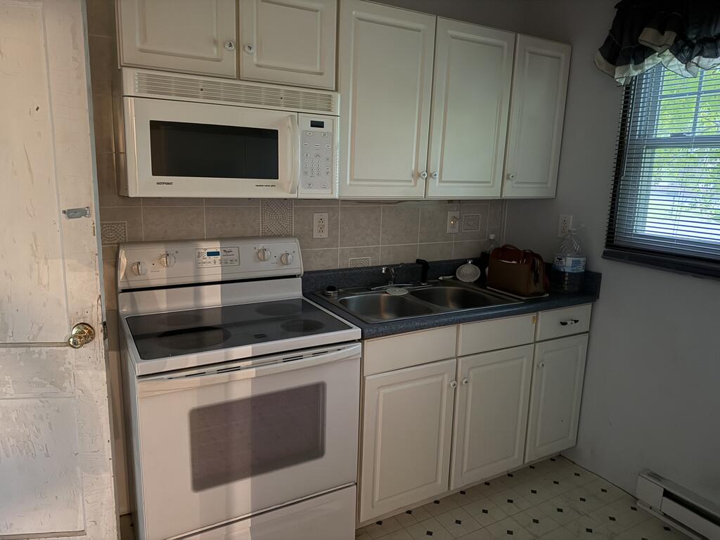 Kitchen with white cabinets, an electric range, and a double-basin sink beneath a window.