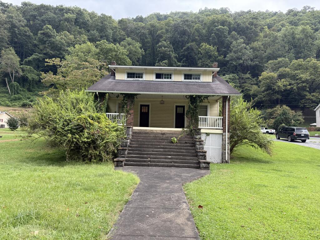 Tan house with a raised porch and broad steps, set against a wooded hillside.