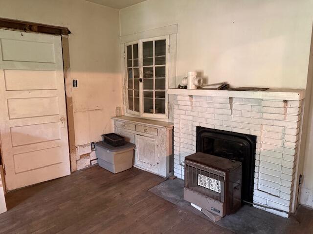 Vacant room with a white brick fireplace, freestanding stove, and built-in cabinet beneath a multi-pane window.