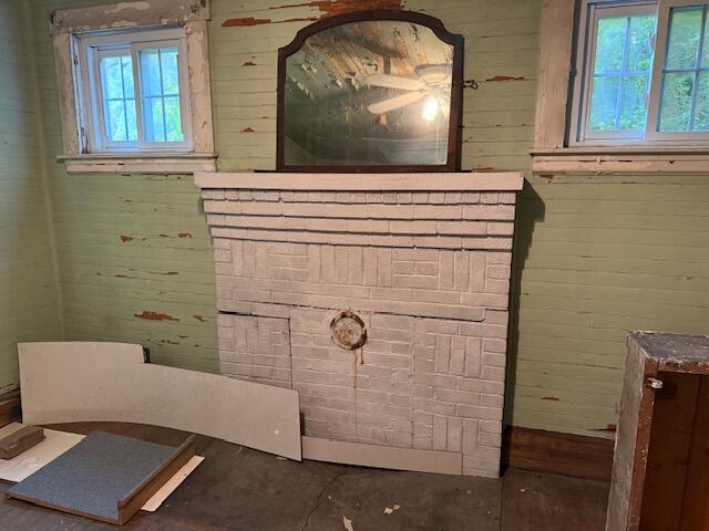 Pale brick fireplace with a mirror above the mantel, flanked by two windows in a room with peeling paint.