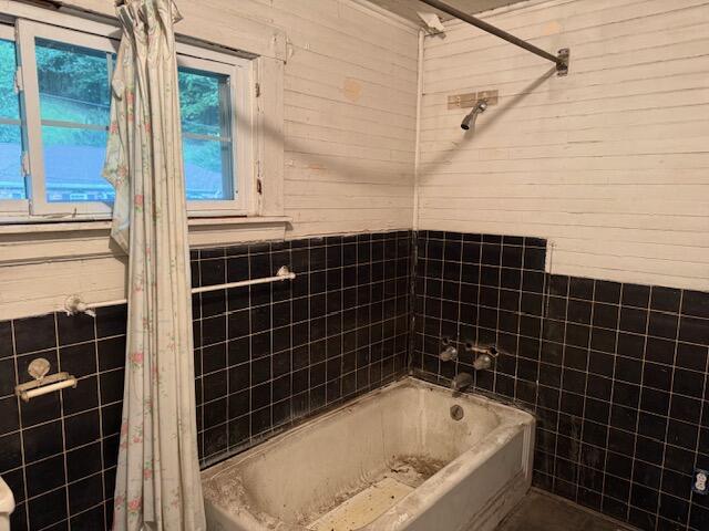Bathroom with a worn bathtub, black tile walls, and two windows.