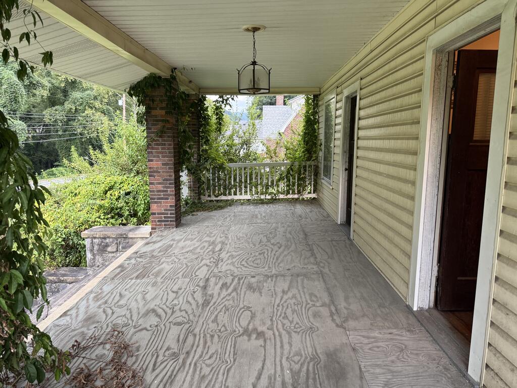 Covered front porch with weathered flooring, a brick column, white railing, and hanging lantern.