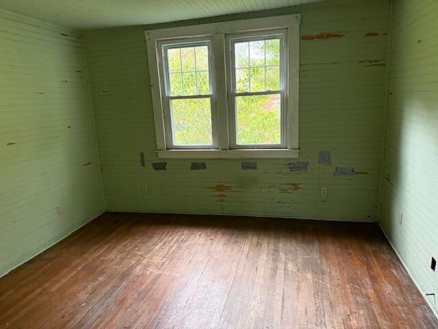 Vacant room with worn pale green walls, hardwood floors, and a double window.