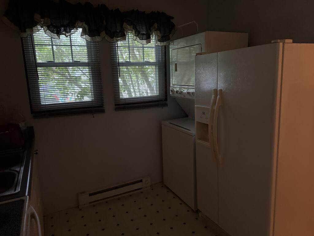 Laundry area with a washer and dryer, large refrigerator, and two windows with blinds.