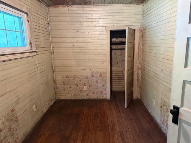 Empty room with worn white paneling, faded floral wallpaper, and dark hardwood floors.