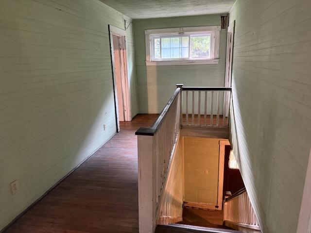 Empty upstairs hallway with hardwood floors, a stair railing, and a window at the end.