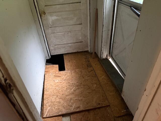 Entryway with plywood floor covering and a dark opening beneath one section.