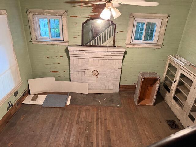 Vacant room with a white brick fireplace, peeling green paint, and exposed hardwood floor.