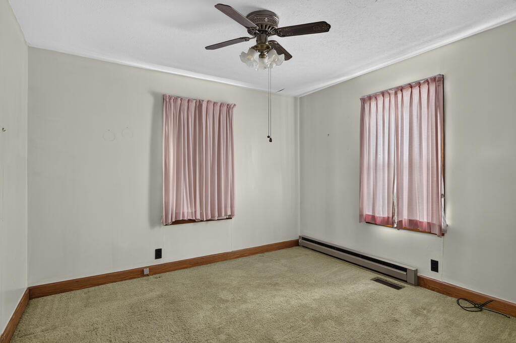 Unfurnished carpeted room with pink curtains, a ceiling fan, and a baseboard heater.