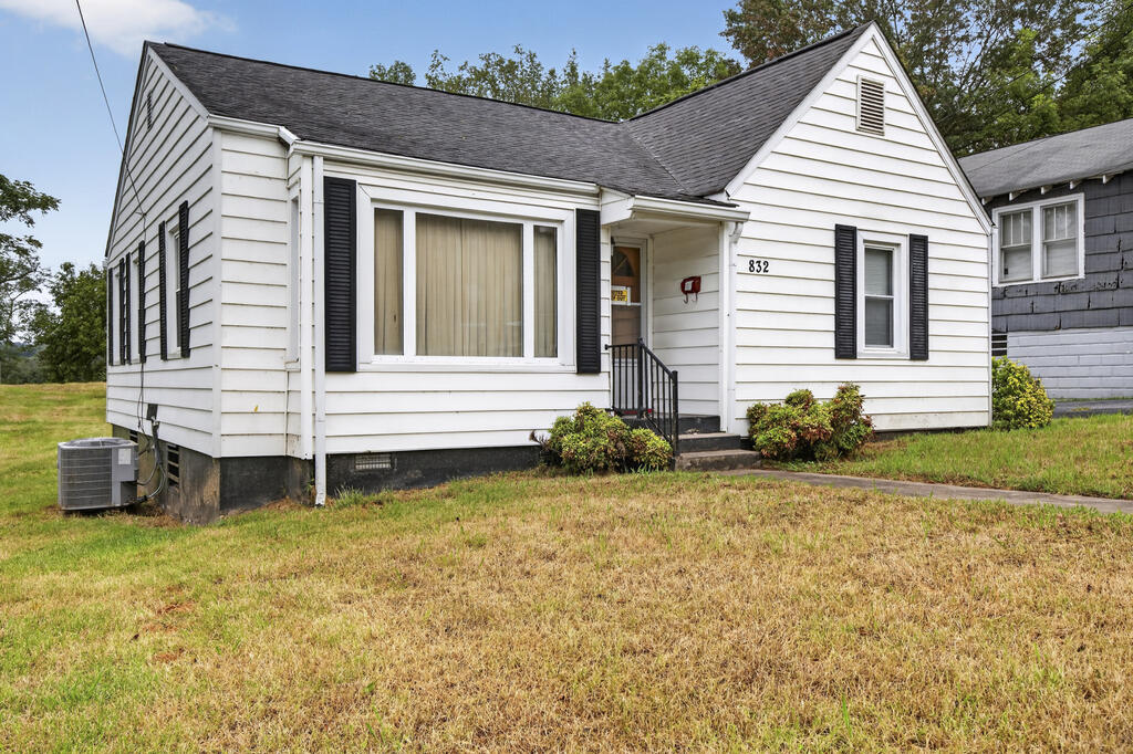 White single-story house with black shutters, a covered entry, and a broad grassy front yard.
