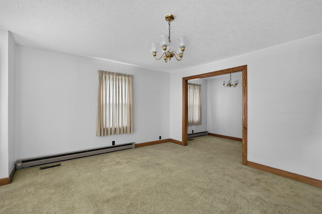 Empty carpeted room with a brass chandelier and wide wood-trimmed opening to an adjoining room.