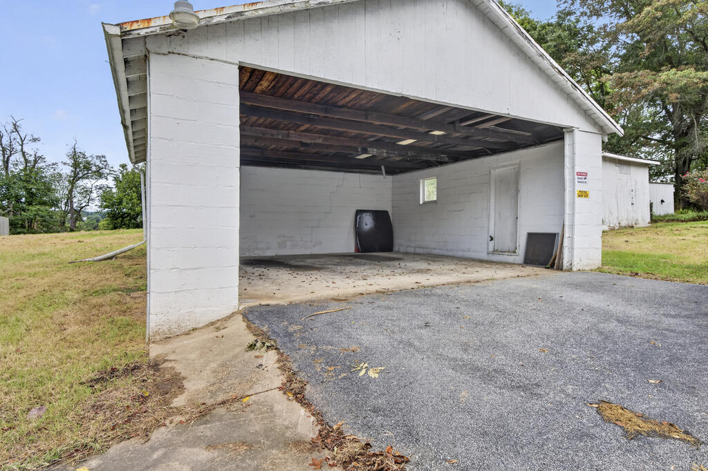 Open-front garage with exposed wooden roof framing, white block walls, and an asphalt driveway.