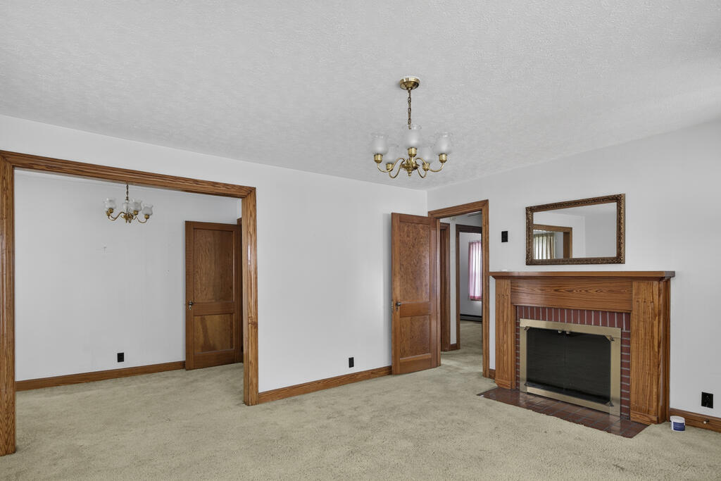 Empty living room with beige carpet, wood-trimmed fireplace, and adjoining doorways.