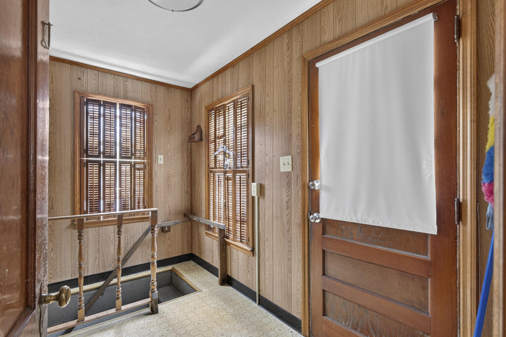 Entryway with wood-paneled walls, shuttered windows, and a wooden door beside a stairwell.