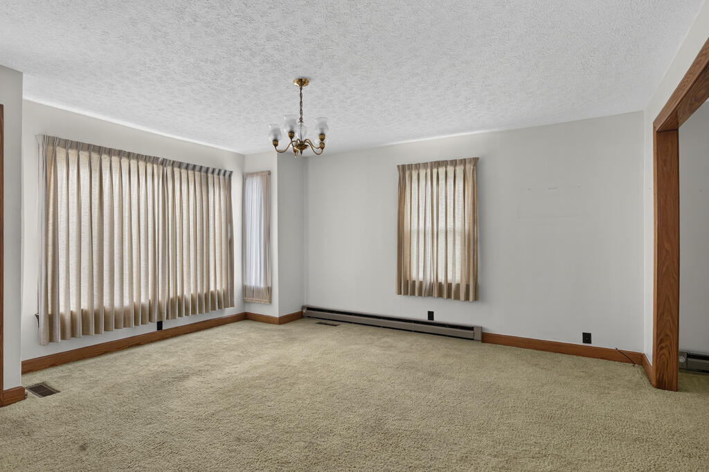 Empty carpeted room with beige curtains, a brass chandelier, and wood trim.