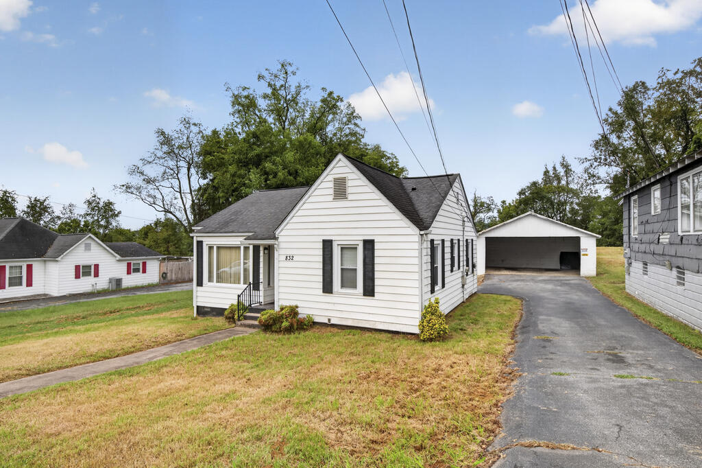 White single-story house with black shutters, a detached garage, and a paved driveway.