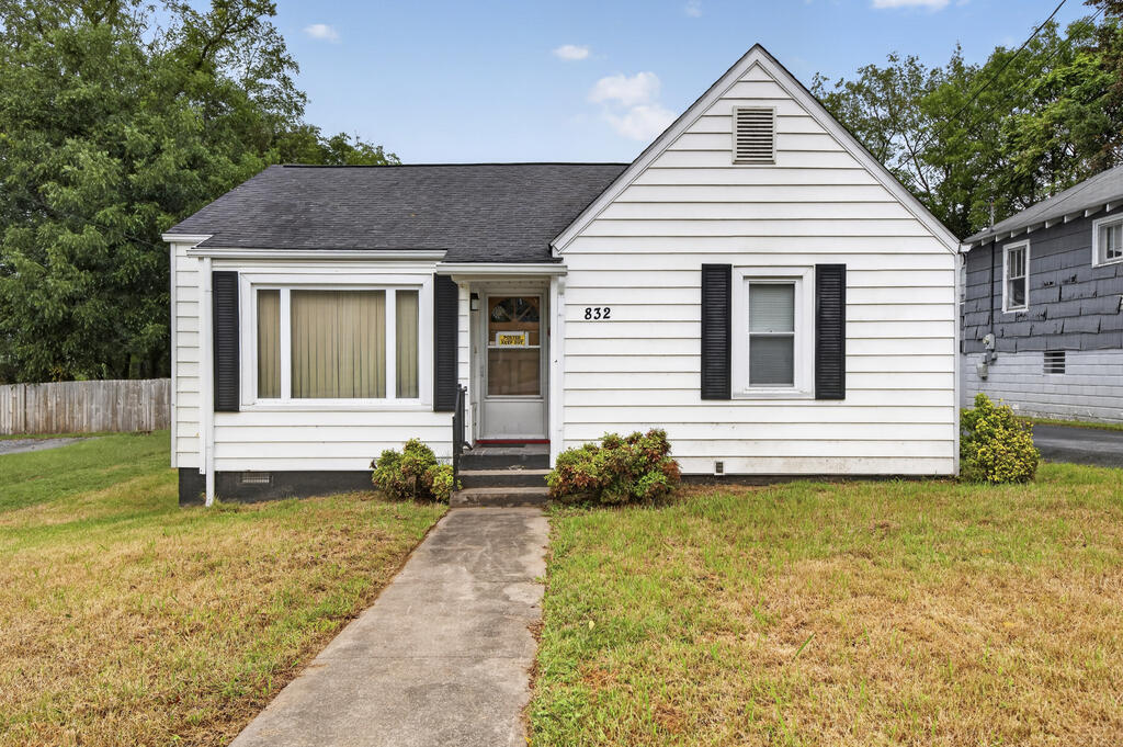 White single-story house with a steep front gable, dark shutters, and a walkway to the entrance.