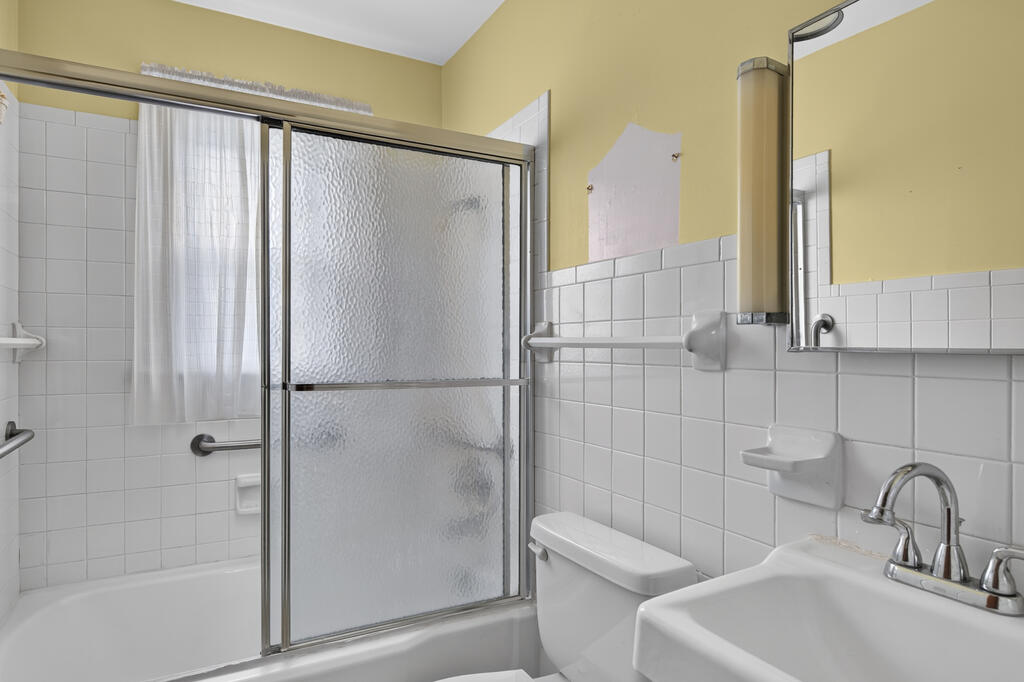 Bathroom with a frosted-glass tub enclosure, white tiled walls, toilet, and pedestal sink.