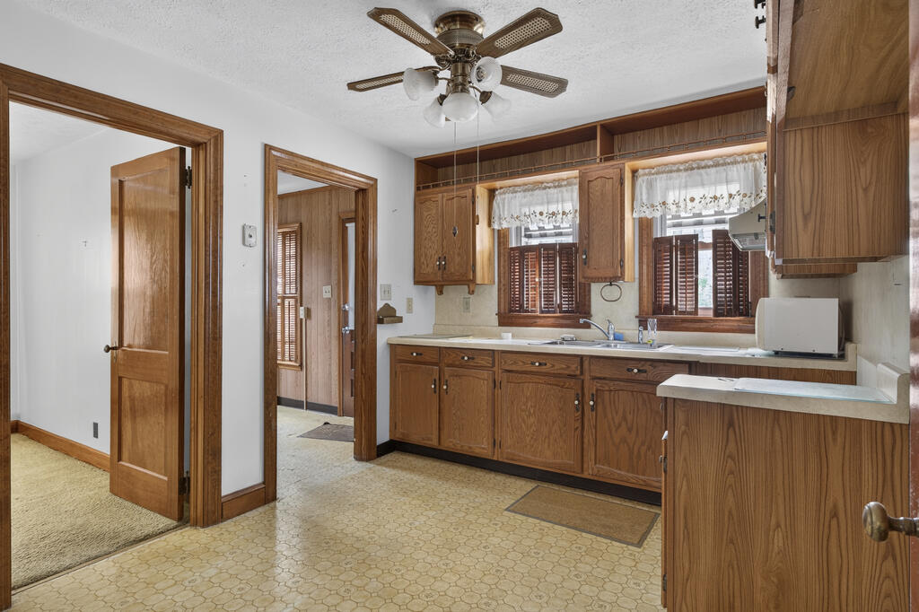 Kitchen with wood cabinetry, a double-basin sink beneath two windows, and patterned vinyl flooring.