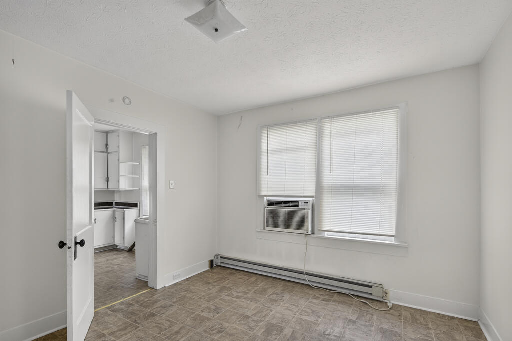 Vacant room with tile flooring, a window air conditioner, and an open doorway to the kitchen.