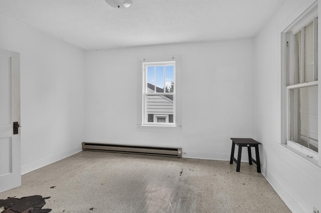 Empty room with two windows, a baseboard heater, and a worn floor.