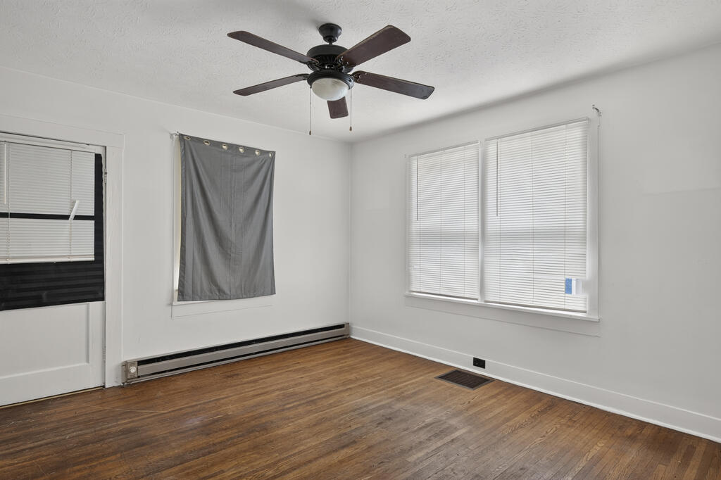 Empty room with hardwood floors, a ceiling fan, and windows with blinds.