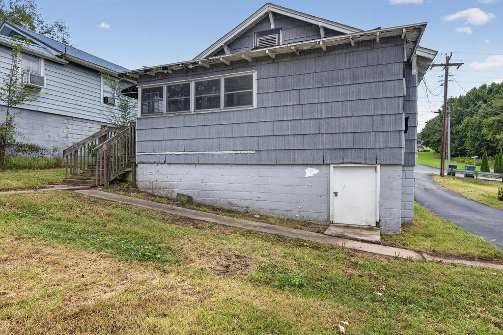 Gray house side with shingle siding, white block foundation, side door, and wooden stairs.