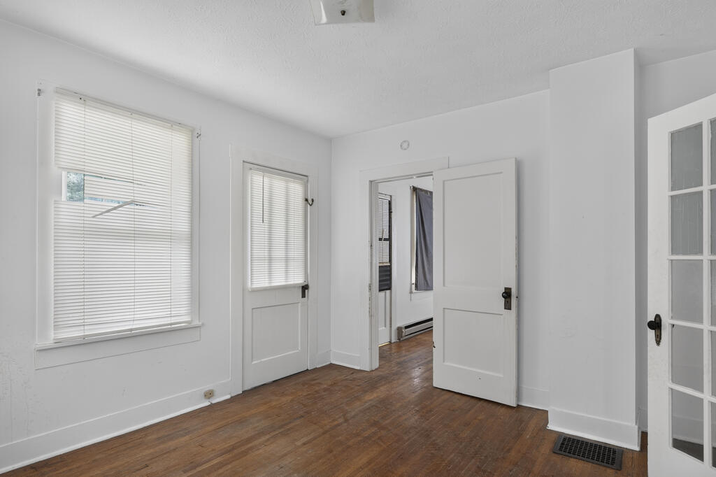 Empty room with hardwood floors, window blinds, and open white doors.