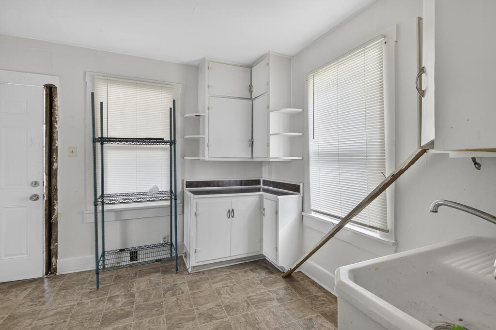 Utility room with white cabinets, a deep sink, wire shelving, and brown tile flooring.