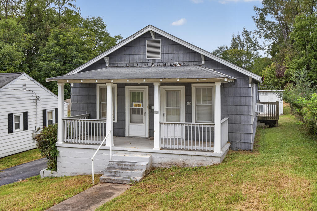 Gray house with a white-railed covered porch and front steps on a grassy lot.