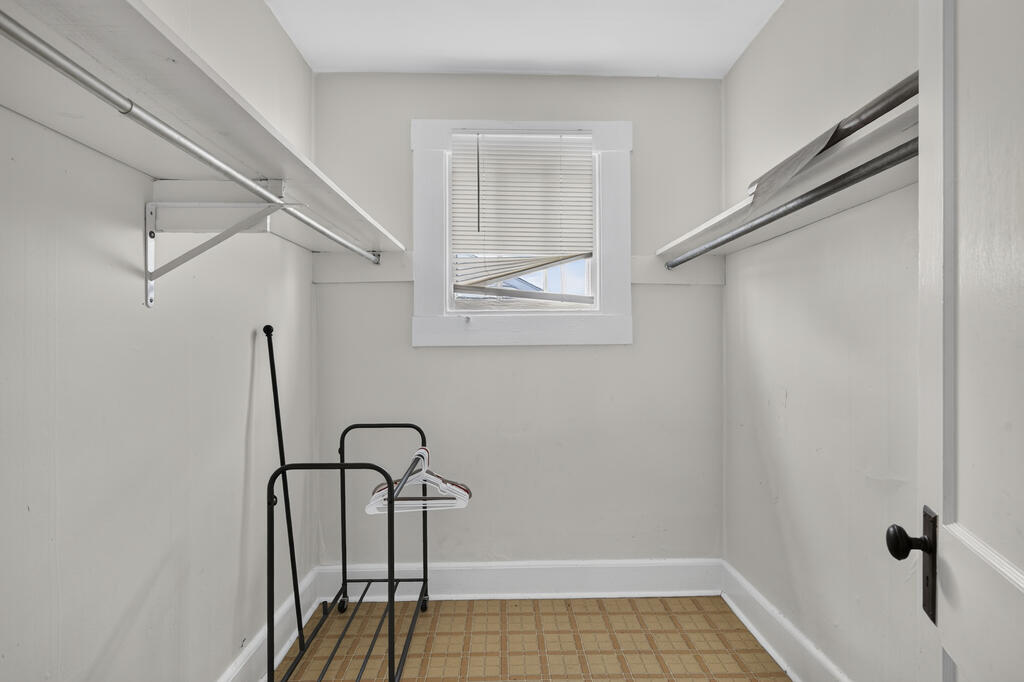 Walk-in closet with metal hanging rods, a high window, and tiled flooring.