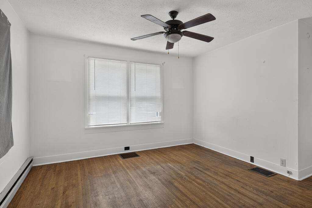 Empty room with hardwood floors, window blinds, ceiling fan, and baseboard heater.