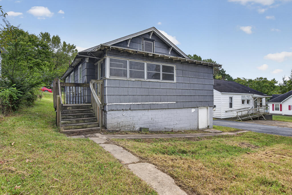 Gray-sided house with a raised wooden porch and stairs, concrete block foundation, and patchy lawn.