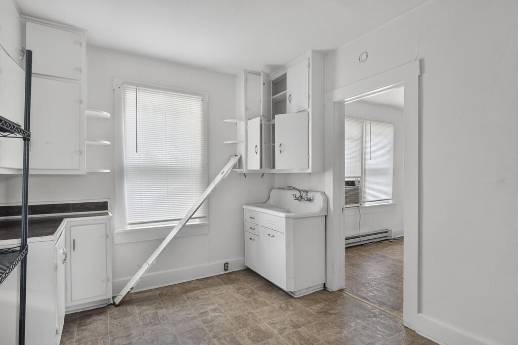 Vacant kitchen with white cabinets, a freestanding sink, and a doorway to a room with a window air conditioner.
