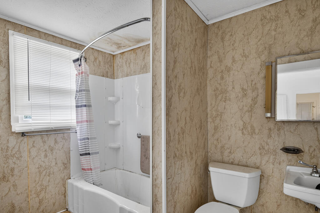 Bathroom with a white tub-shower, striped curtain, toilet, and mottled tan walls.