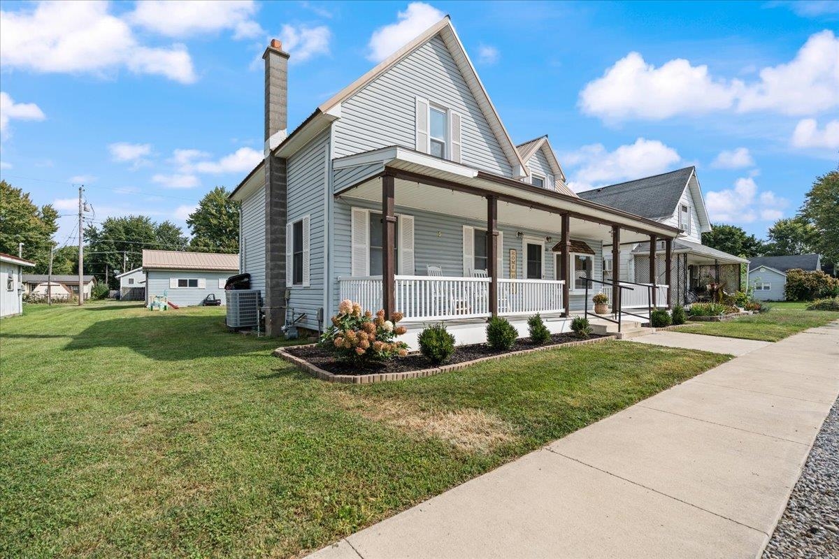 Light blue-gray two-story house with a long covered porch, white railings, and landscaped flower bed.