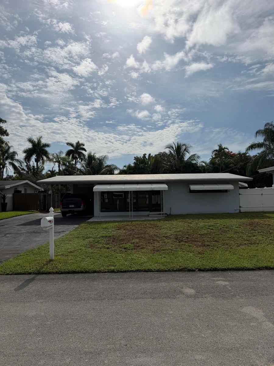Single-story white house with a broad lawn, driveway, mailbox, and palm trees.