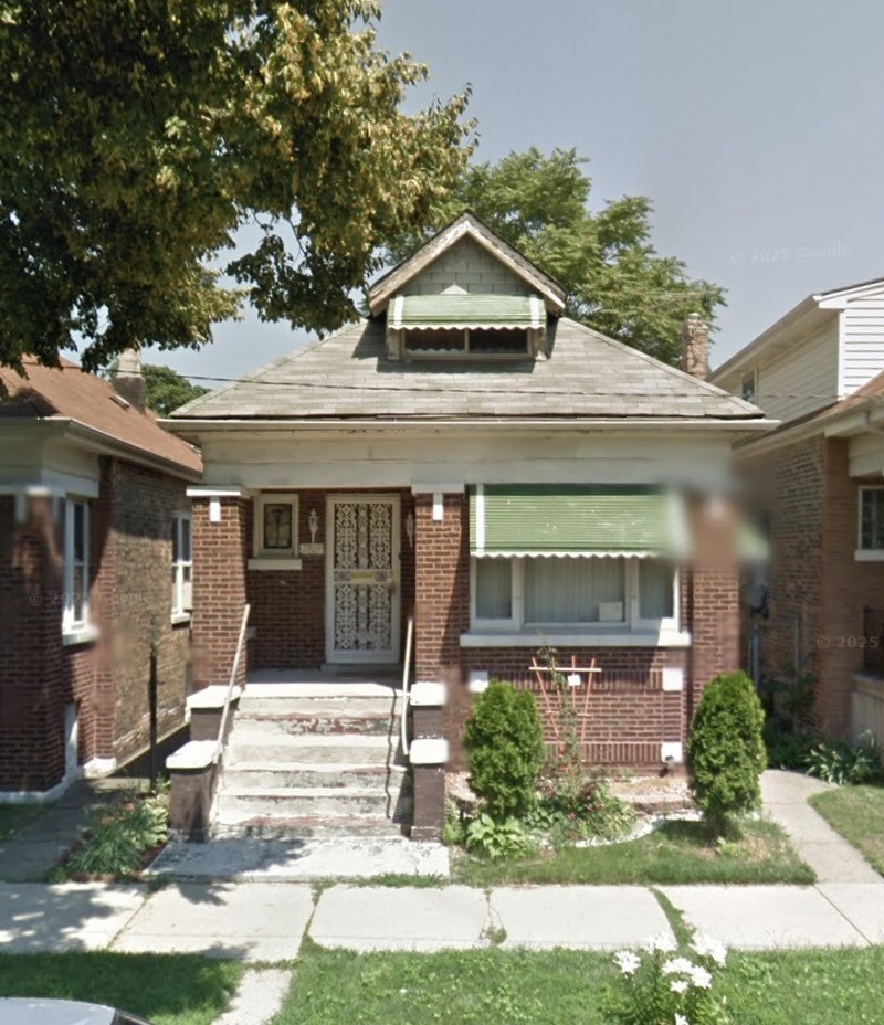 Red-brick bungalow with a front dormer, green window awning, and raised entry steps.