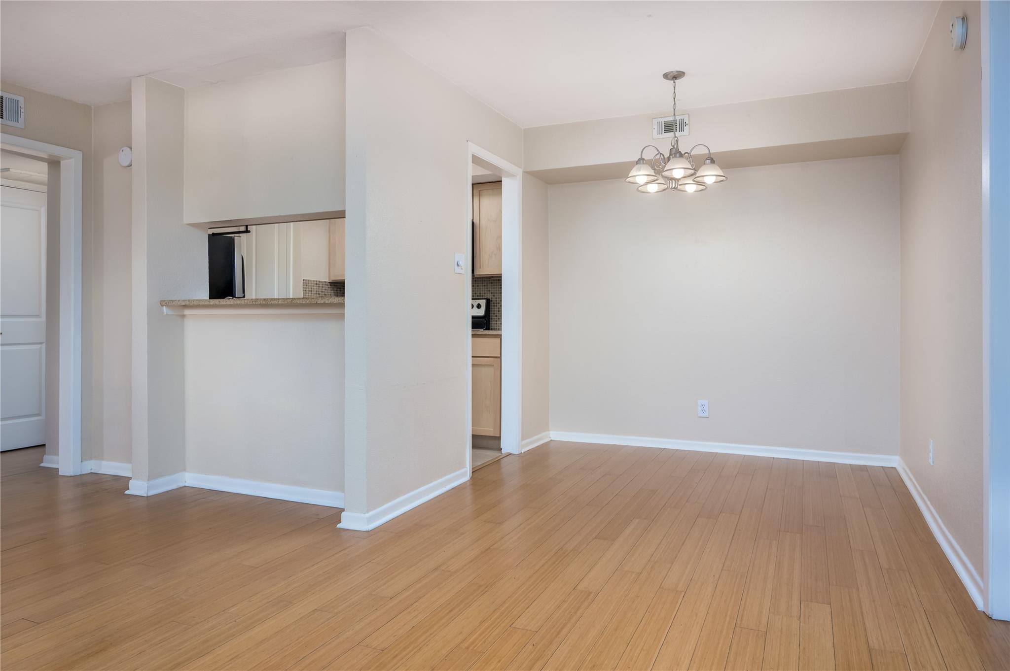 Empty dining area with light wood floors, a chandelier, and a kitchen pass-through.
