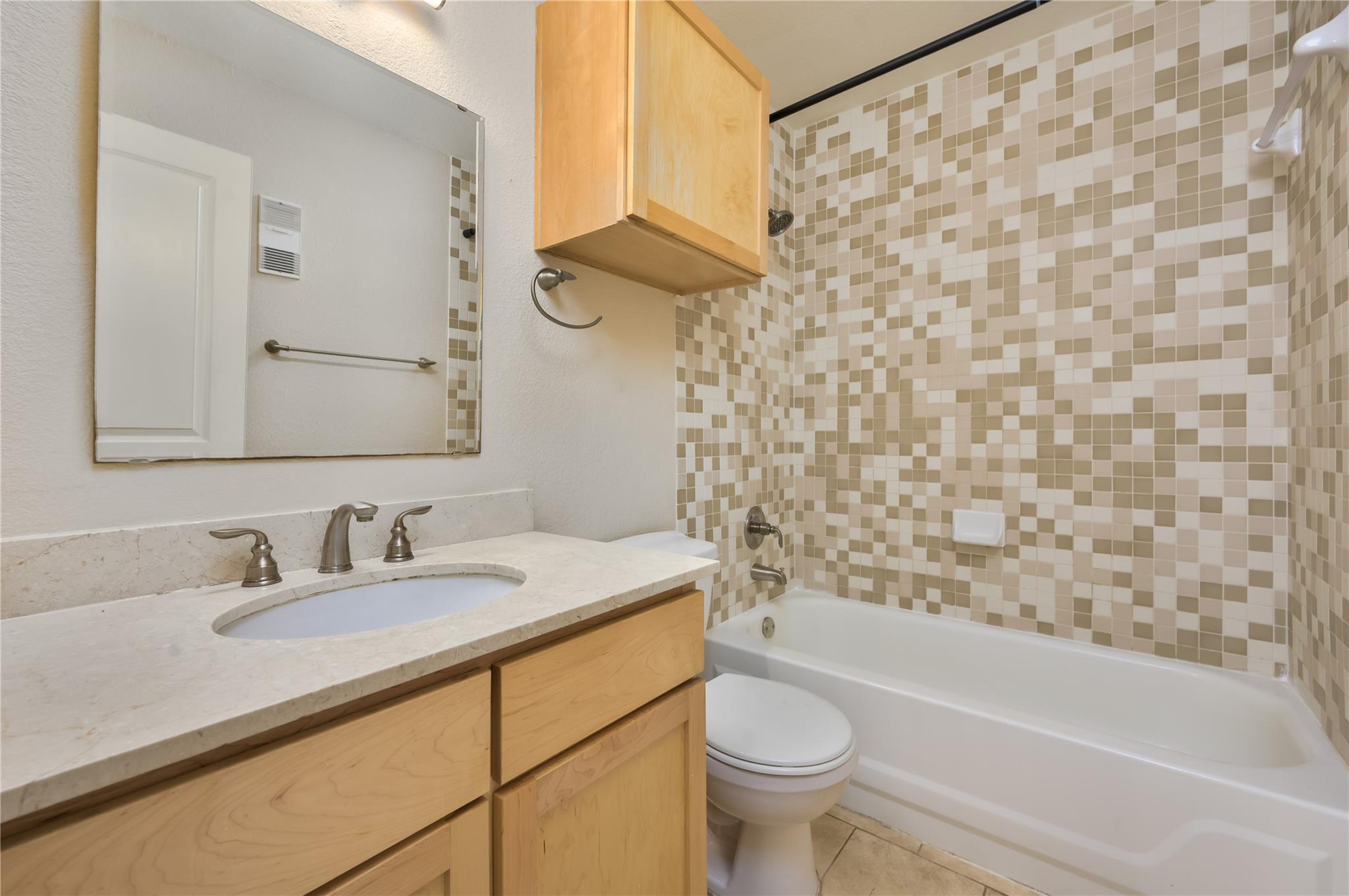 Bathroom with a wood vanity, inset sink, and mosaic-tiled tub surround.