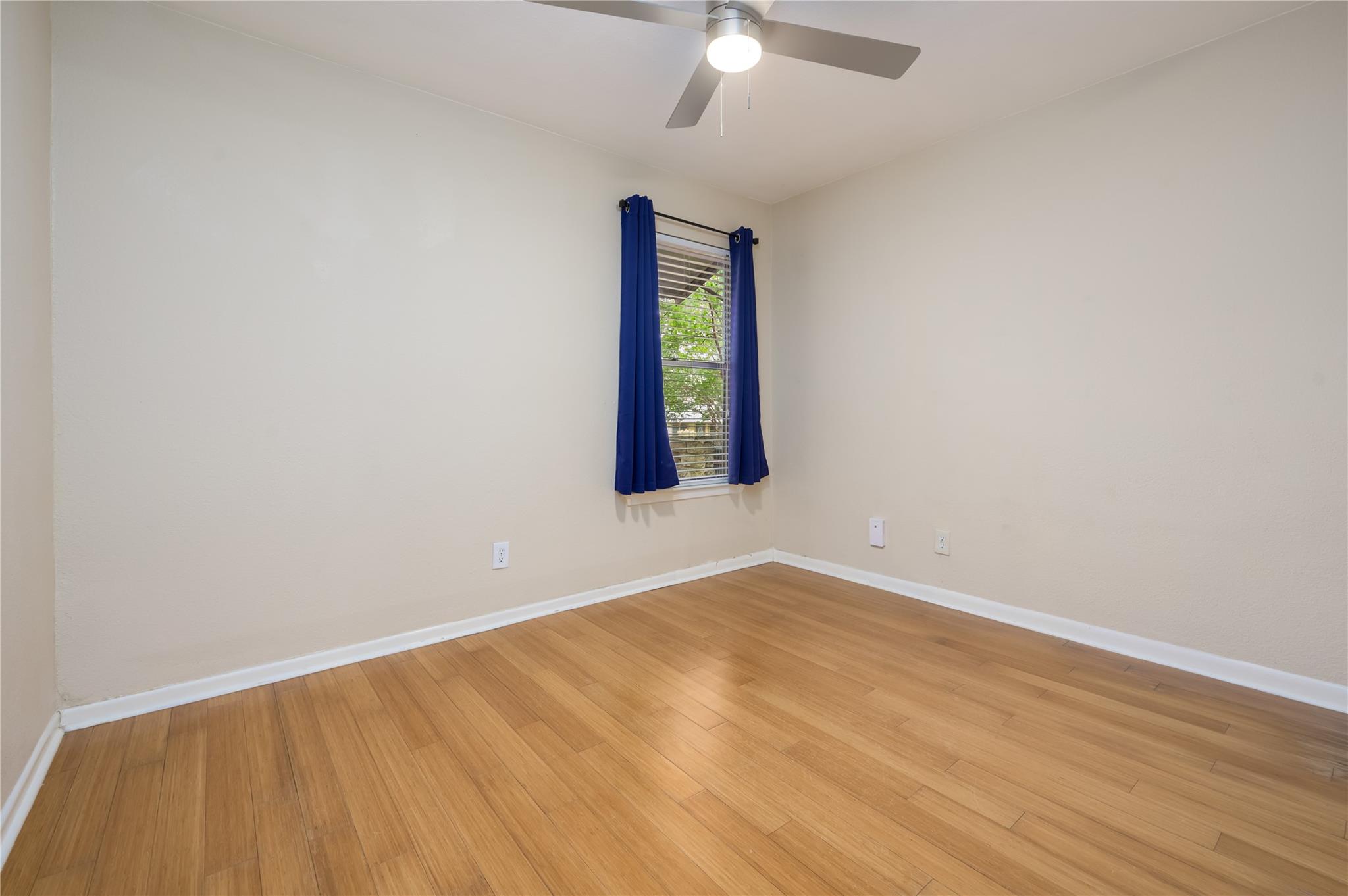 Empty bedroom with wood flooring and a window framed by blue curtains.