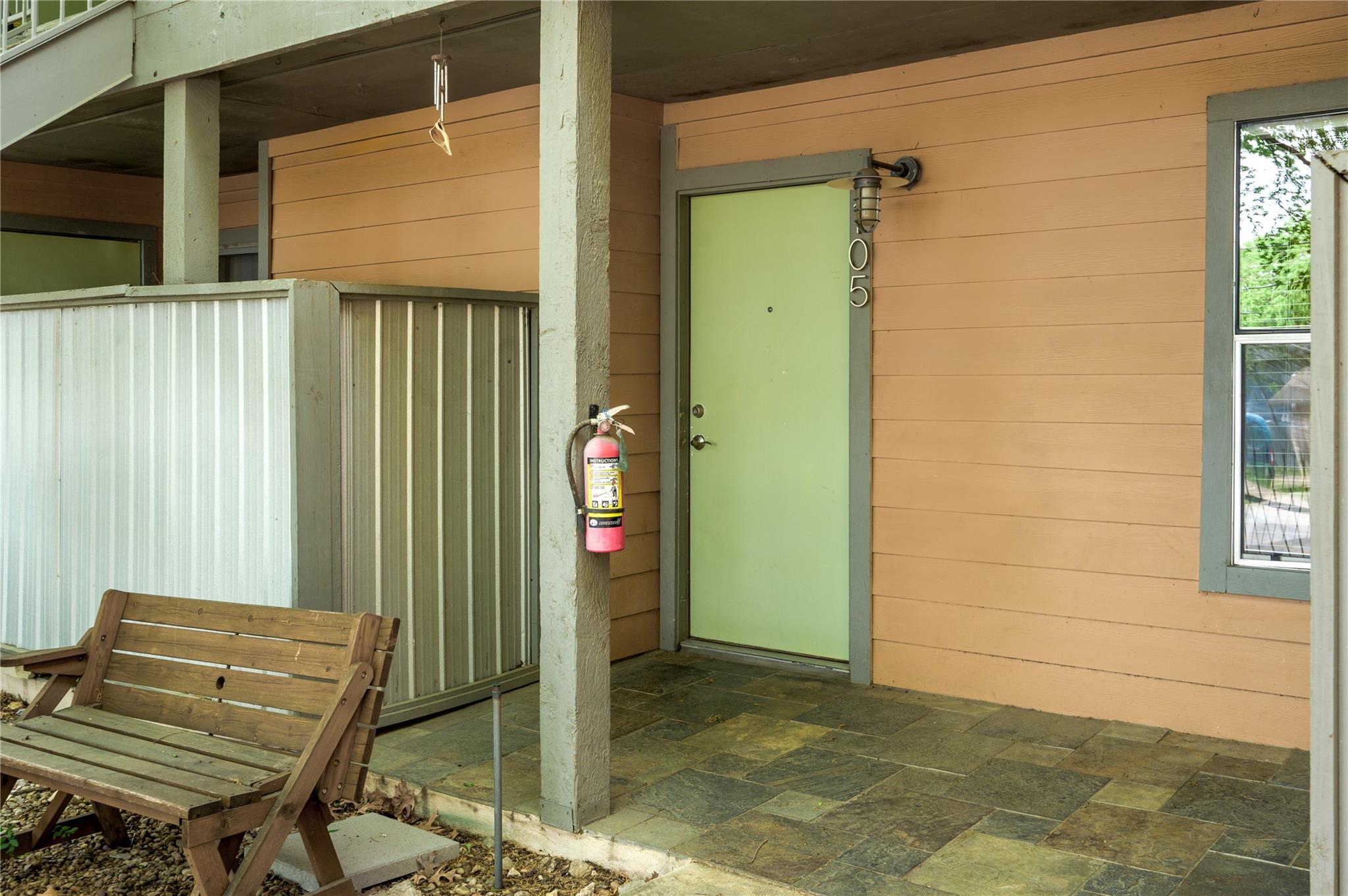 Covered home entrance with green door marked 105, tiled porch, and wooden bench.