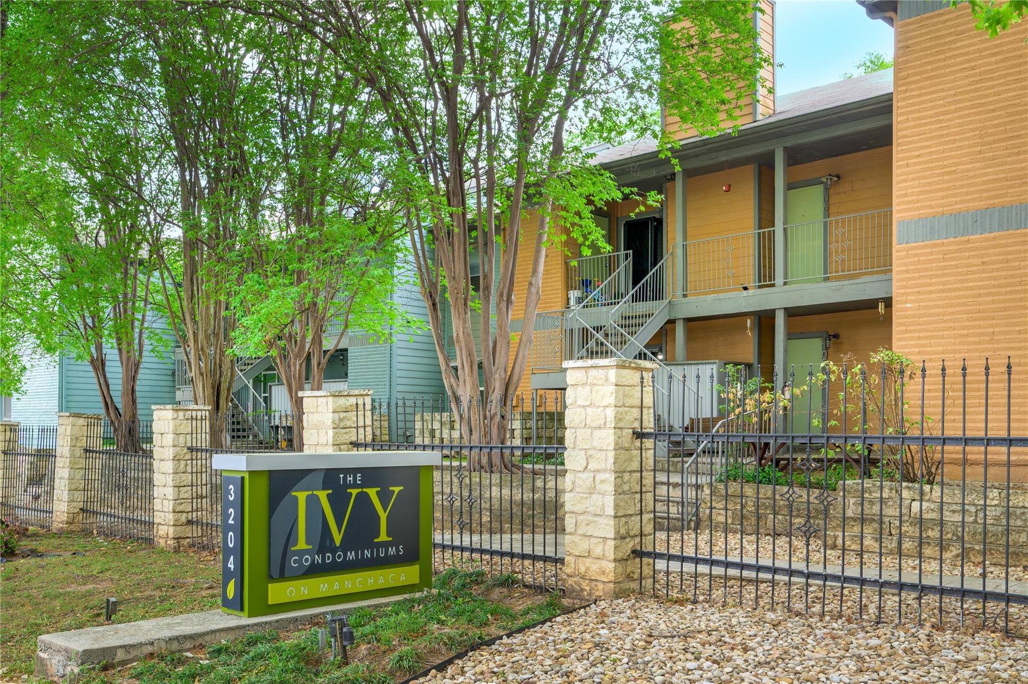 Condominium building behind a stone wall and iron fence, with a sign for The Ivy on Manchaca.