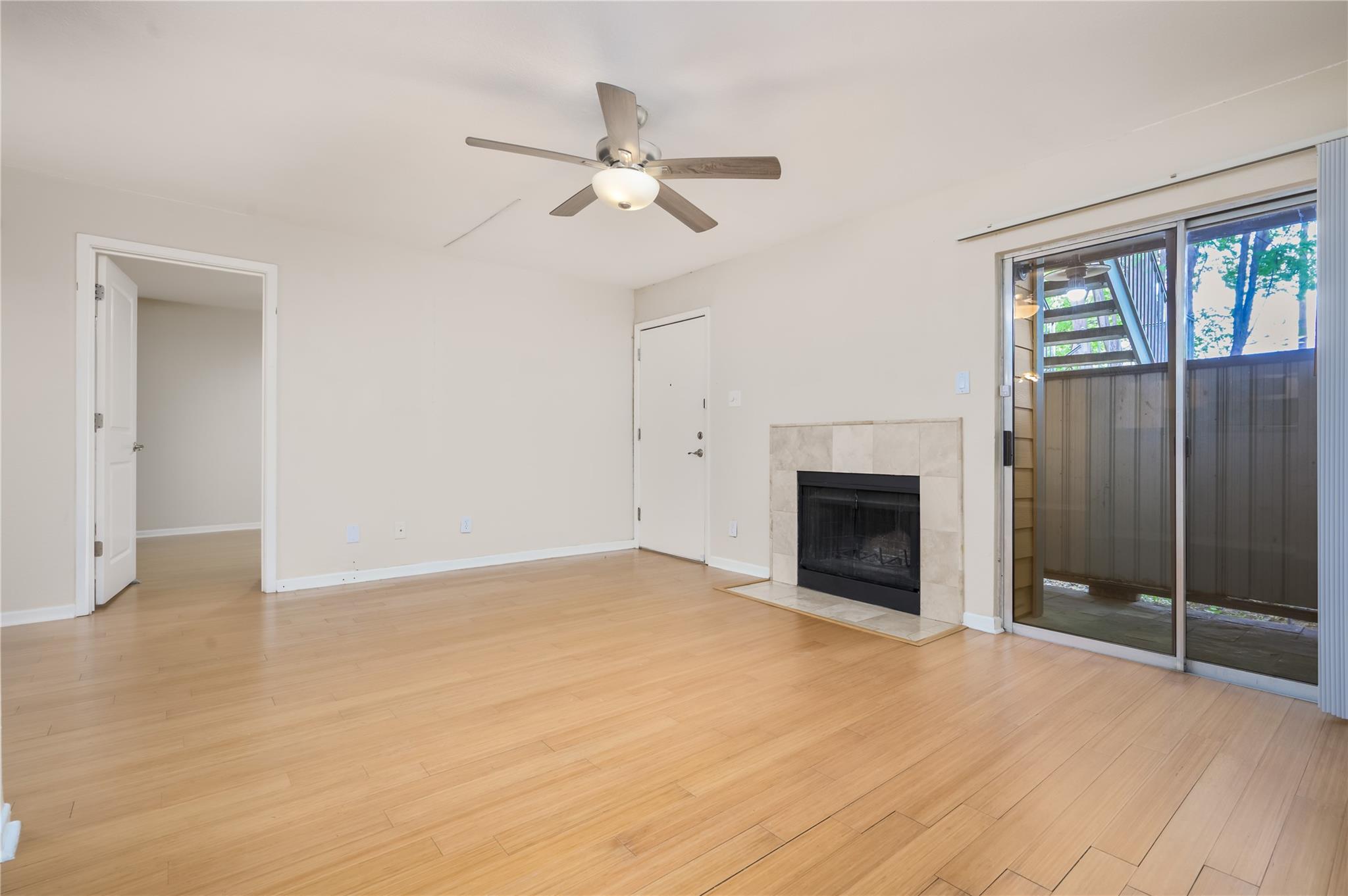 Empty living room with a tiled fireplace, ceiling fan, and sliding glass doors to a balcony.