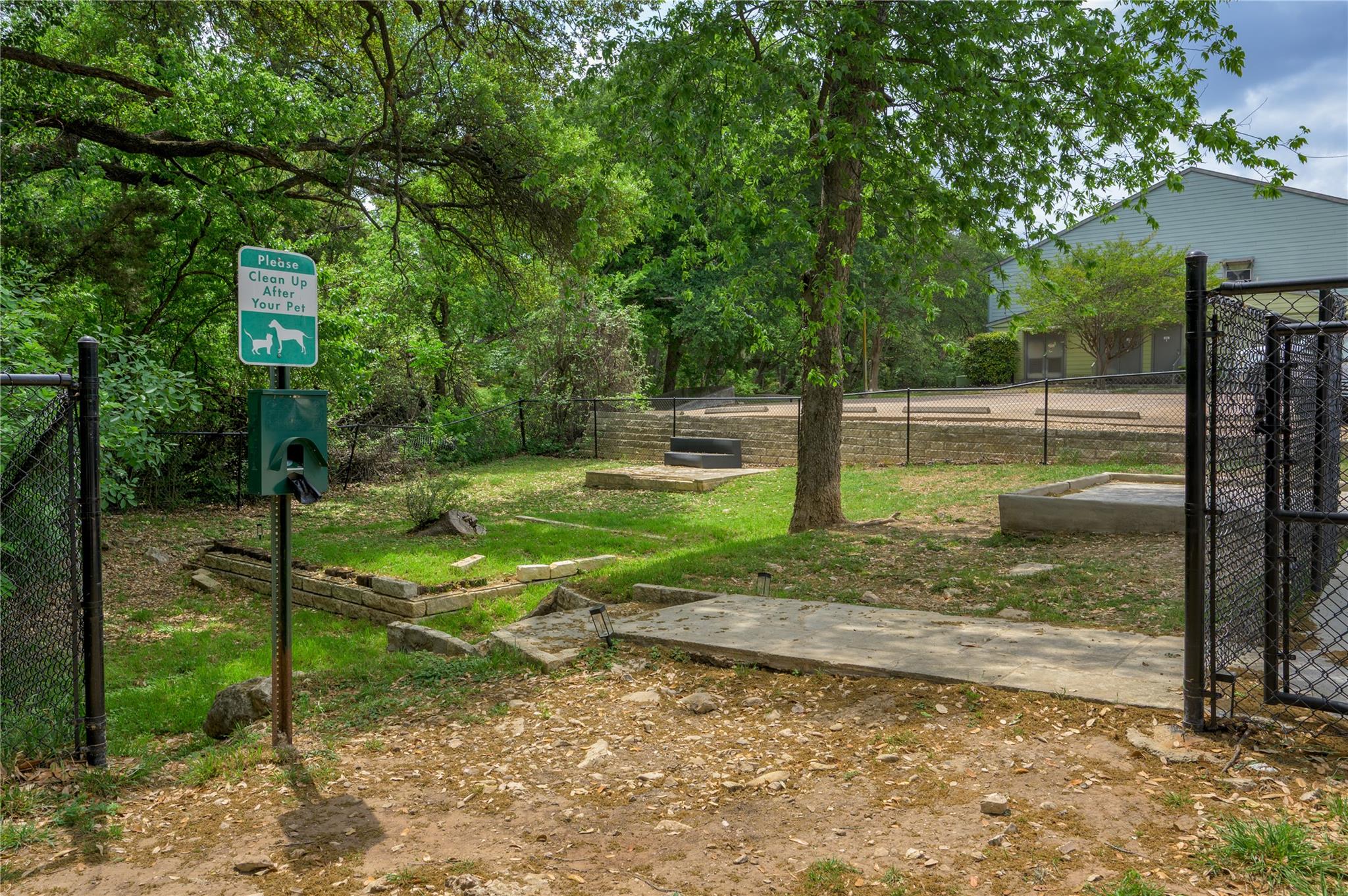 Fenced residential pet area beneath mature trees, with a pet waste station and concrete pads.